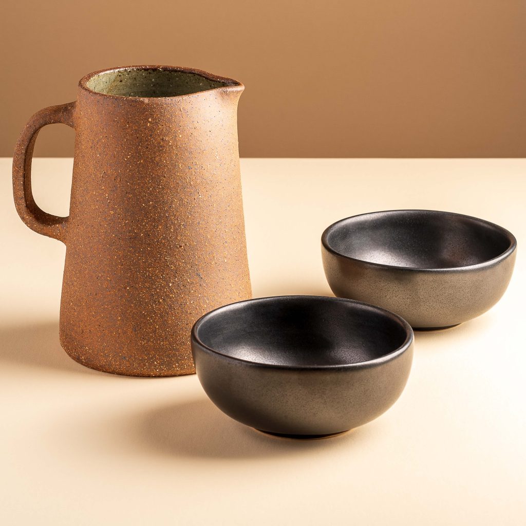Product photograph of an earthenware jug and two black, ceramic bowls.
